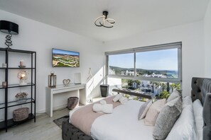 A modern bedroom with a large bed, a desk, and a view of a cityscape through a large window. - Apartment Stay at Alcazaba Lagoon (Casares)