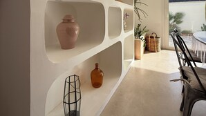 Ein modernes Interieur mit einer weißen Wand mit eingelassenen Regalen, einem Essbereich mit Tisch und Stühlen sowie Blick ins Freie.
