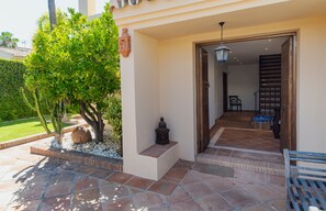 A covered outdoor area with a tiled floor, a bench, and a door leading to an interior space. - Charming Andalusian Beach Villa (Marbella)