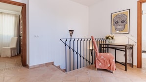 Un escalier avec une rampe en métal, une chaise, une table avec un vase de fleurs et un tableau encadré au mur.