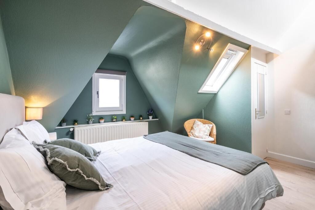 Un dormitorio con techo inclinado, una cama con almohadas, una silla, un radiador y una ventana.