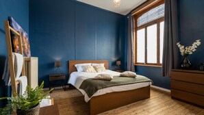 A bedroom with a wooden bed, a nightstand, a dresser, a window with curtains, and a potted plant. - The Canal View Suites (Bruges)