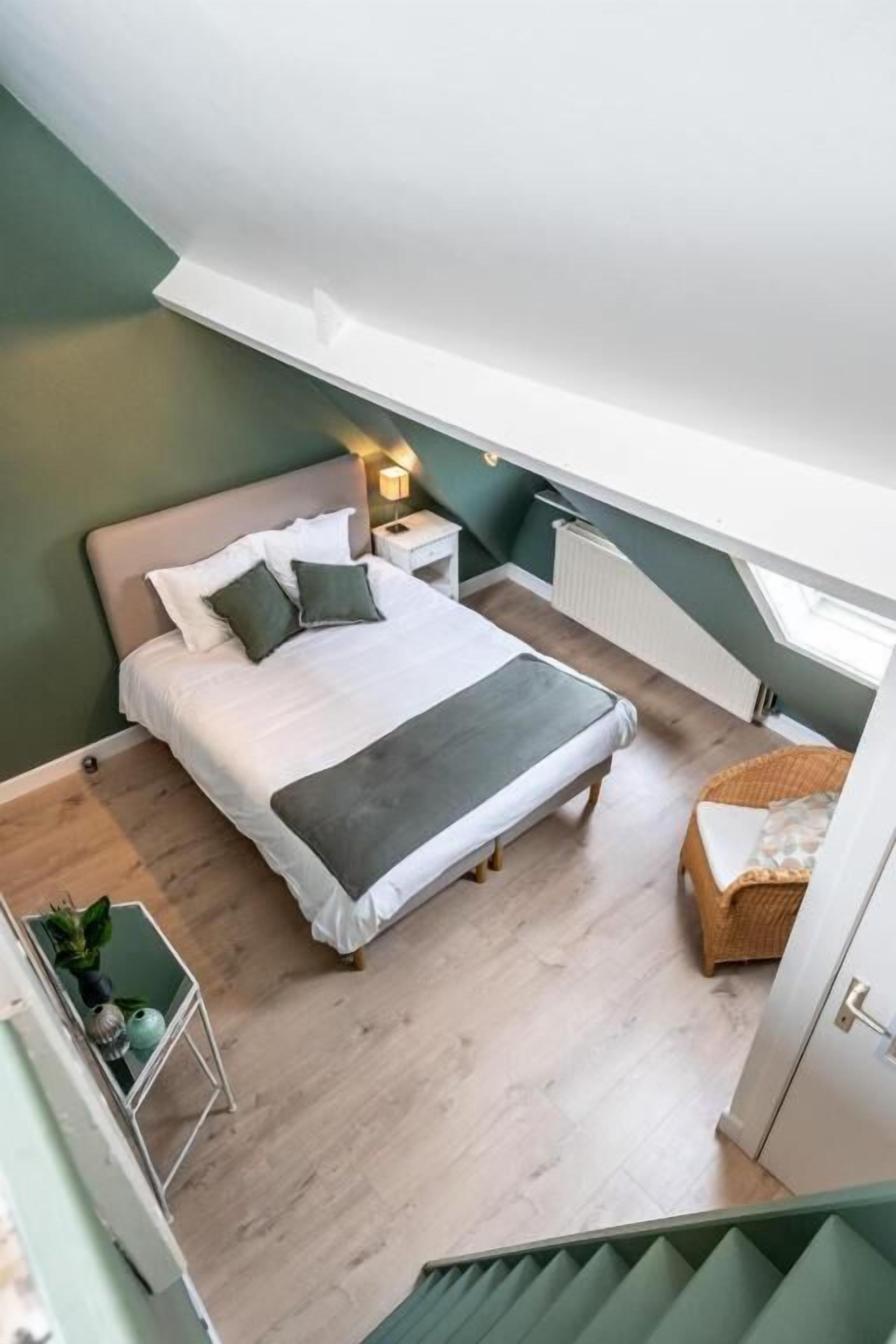 A bedroom with a bed, bedside tables, a radiator, a window, and a staircase.
