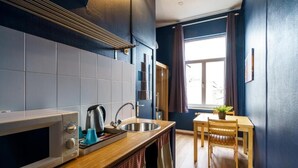 A compact kitchen with a microwave, kettle, and sink. There's a wooden table with a chair and a window with curtains. - The Canal View Suites (Bruges)