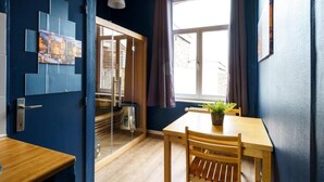 A room with a wooden table and chairs, a window with curtains, and a wall with a geometric art piece. - The Canal View Suites (Bruges)