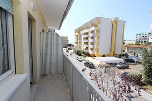 Ein Balkon mit Blick auf ein mehrgeschossiges Gebäude, das ebenfalls Balkone, einen Parkplatz und einen klaren Himmel zeigt.