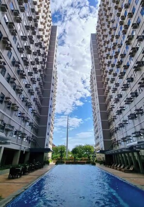 Un immeuble résidentiel moderne doté d’une piscine centrale, entouré de balcons et d’espaces de détente en plein air.