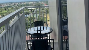 A balcony with a table and chairs, a view of a cityscape, and a clear sky. - Lux 2BR Sky Condo With 24-hr Security, Fully Airconditoned & Basement Parking (Dasmarinas)