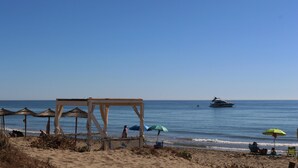 Uma praia com uma estrutura de madeira, guarda-sóis e um barco na água.