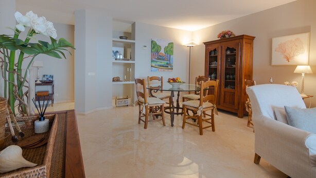 Uma sala de estar com uma mesa de jantar, cadeiras, um sofá, um armário e um quadro na parede.
