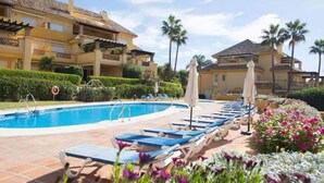 Piscina com espreguiçadeiras e guarda-sóis, cercada por sebes e flores bem cuidadas.