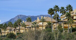 A row of yellow buildings with palm trees in front, set against a mountain backdrop. - Elegant Seafront Retreat in Rio Real Playa (Marbella)