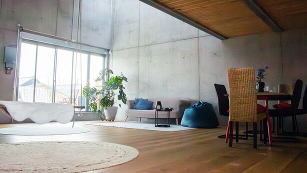 Een ruime woonkamer met een groot raam, een plant in pot, een bank, een salontafel en een eethoek met stoelen en een tafel.