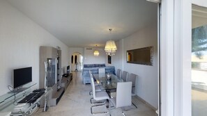 A modern living room with a TV, entertainment unit, sofa, dining table, and chairs. - Cozy Elviria Beachside Apartment (Marbella)