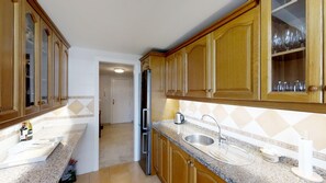 A kitchen with wooden cabinets, a stainless steel sink, and a granite countertop. - Cozy Elviria Beachside Apartment (Marbella)