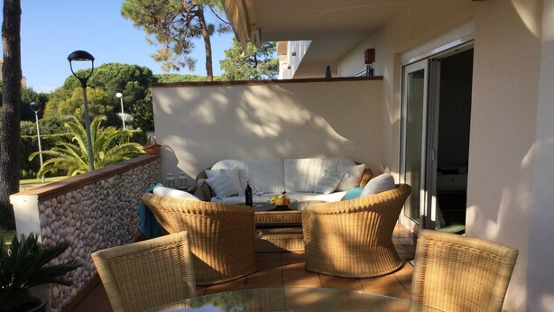 Eine sonnendurchflutete Terrasse mit Korbmöbeln, einem Glastisch und Blick auf einen üppigen Garten.