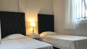 Ein Hotelzimmer mit zwei Einzelbetten, einem Nachttisch mit Lampe und einem Fenster mit Vorhängen.