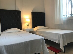 A hotel room with two single beds, a nightstand with a lamp, and a window with curtains. - Cozy Elviria Beachside Apartment (Marbella)