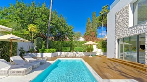 Ein Pool mit Liegestühlen und Sonnenschirmen, umgeben von Grünflächen und einem modernen Gebäude.