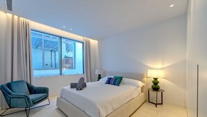 Ein modernes Schlafzimmer mit einem großen Bett, einem blauen Sessel und einem Nachttisch mit Lampe.
