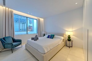 A modern bedroom with a large bed, a blue armchair, and a nightstand with a lamp. - Spacious Villa for 12 in Puerto Banus (Marbella)