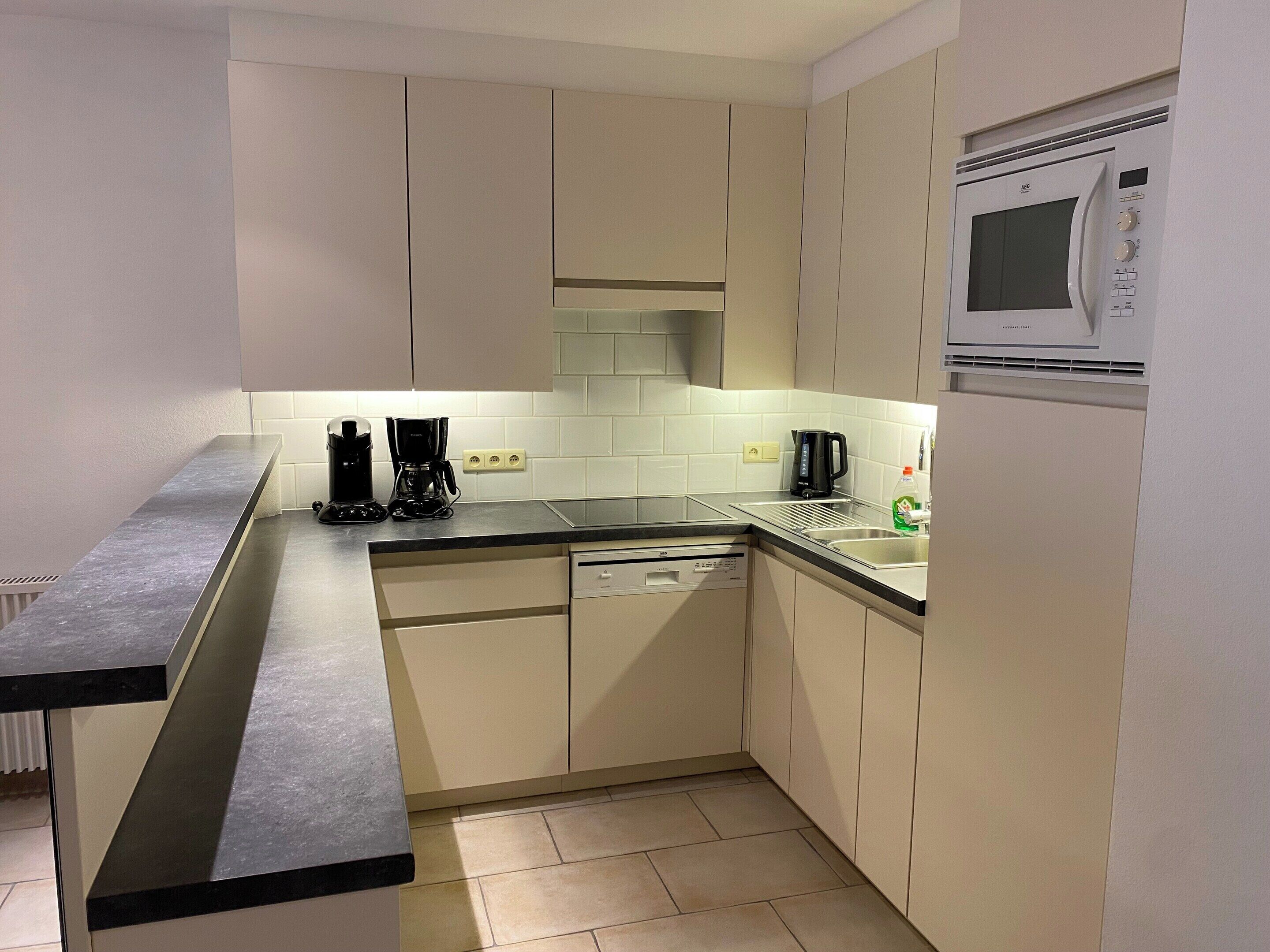A modern kitchen with a dishwasher, a coffee maker, and a microwave.