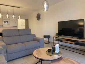 Een moderne woonkamer met een grijze bank, een ronde salontafel met een dienblad, een flatscreen televisie en hanglampen.