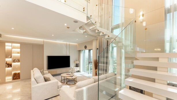 A modern living room with a large flat-screen TV, a sofa, and a glass staircase. - PVH - Central Park 1BR with Study Room (Dubai)