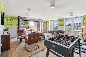 A modern room with a foosball table, comfortable seating, and large windows offering city views. - Landing Apartments Fort Worth near Cultural District (Fort Worth)