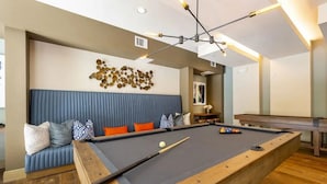 A pool table with a blue cushioned seating area, a billiards cue, and a decorative wall piece. - Landing Amazing 1bd, Courtyard, Game Room (Houston)