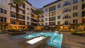 A multi-story hotel with a swimming pool, outdoor seating, and palm trees. - Landing Amazing 1bd, Courtyard, Game Room (Houston)