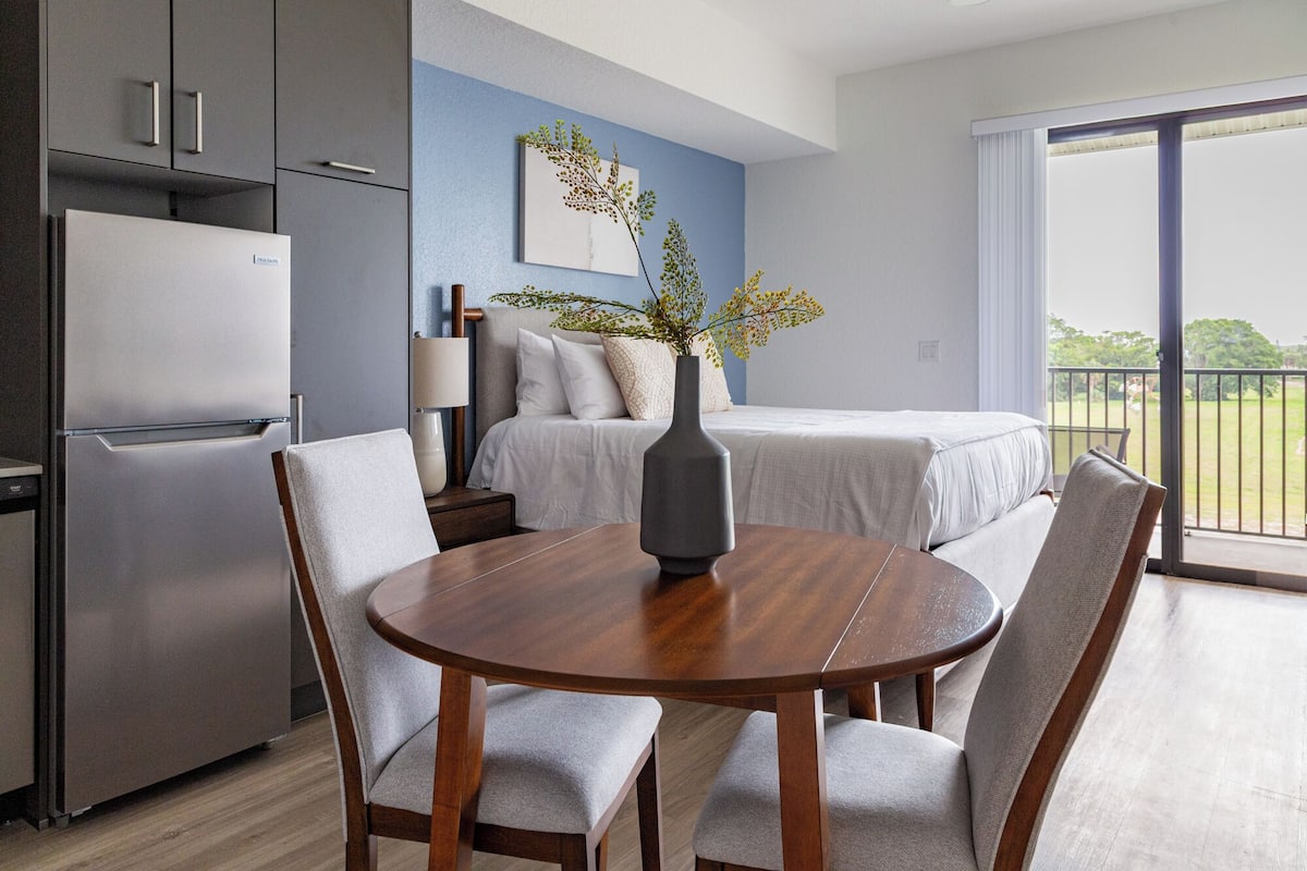 Une chambre d’hôtel moderne comprenant un coin repas, un lit, une table de chevet, une lampe et une vue sur l’extérieur.