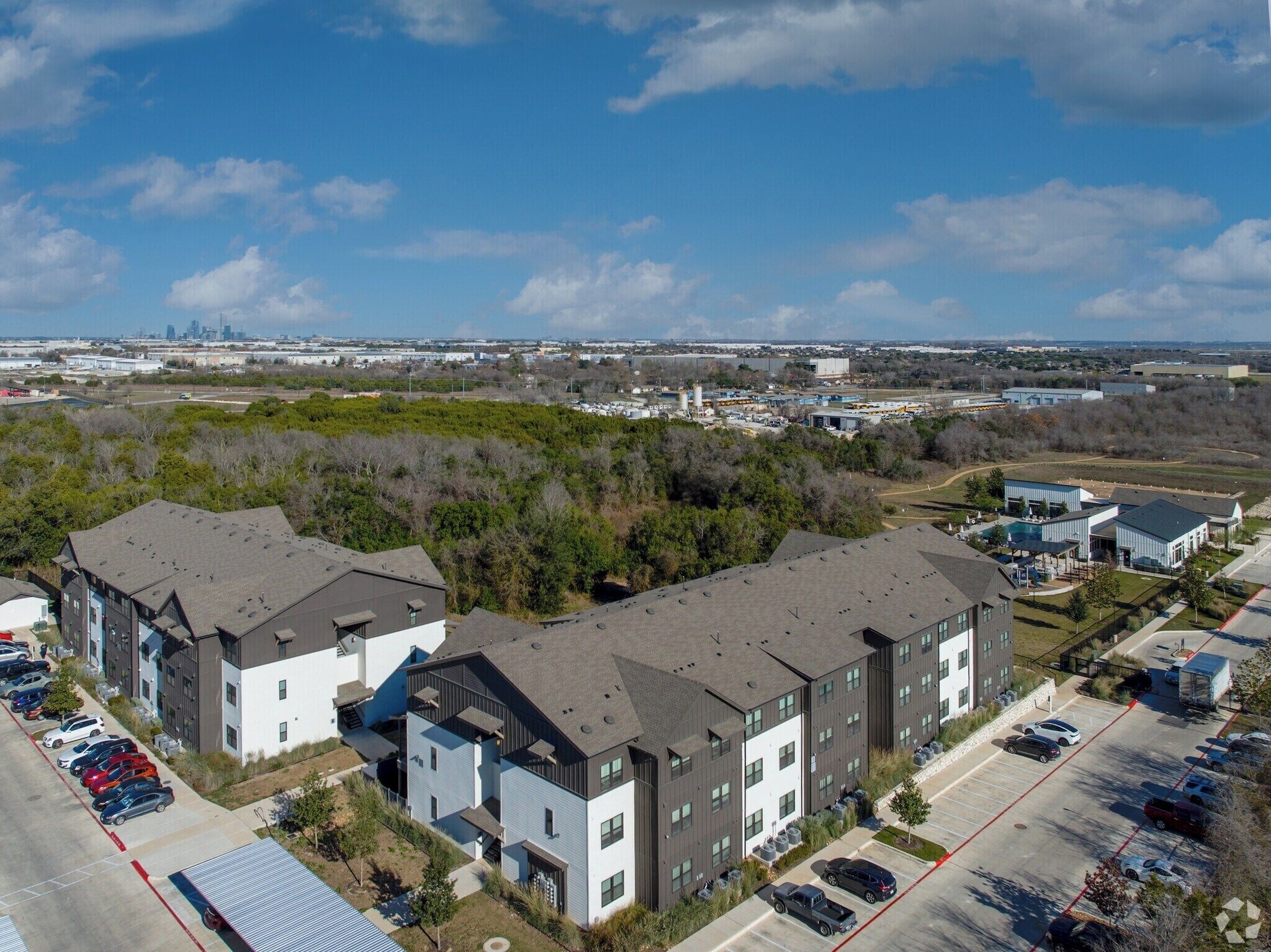 A multi-story residential building with a parking lot and a view of a city skyline.