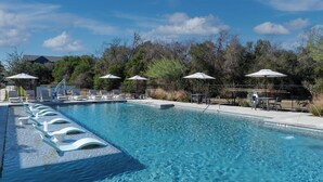 A swimming pool with lounge chairs and umbrellas, surrounded by trees and a clear sky. - Landing Apartments - Southeast Austin (Austin)