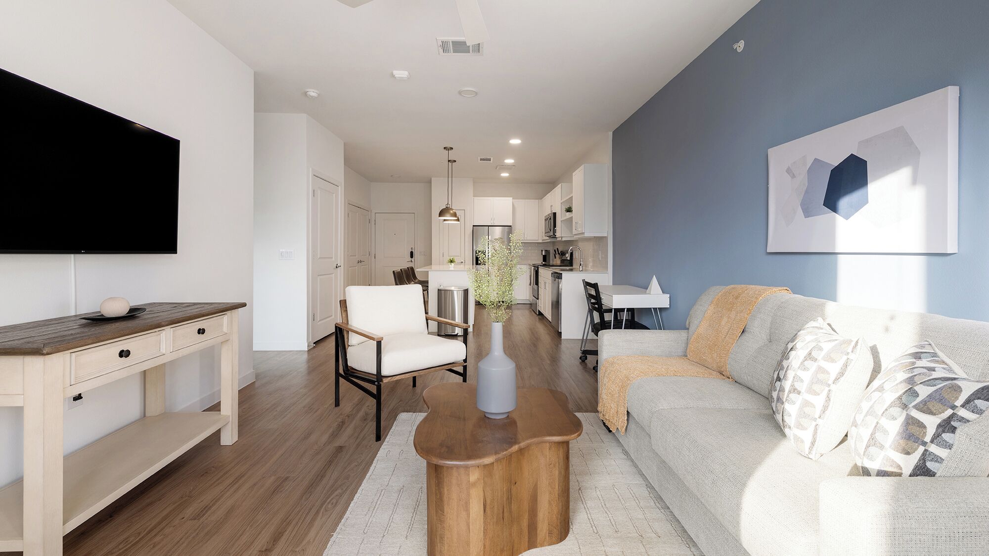 A modern living room with a flat-screen TV, wooden coffee table, white sofa, and a dining area with a white table and chairs.