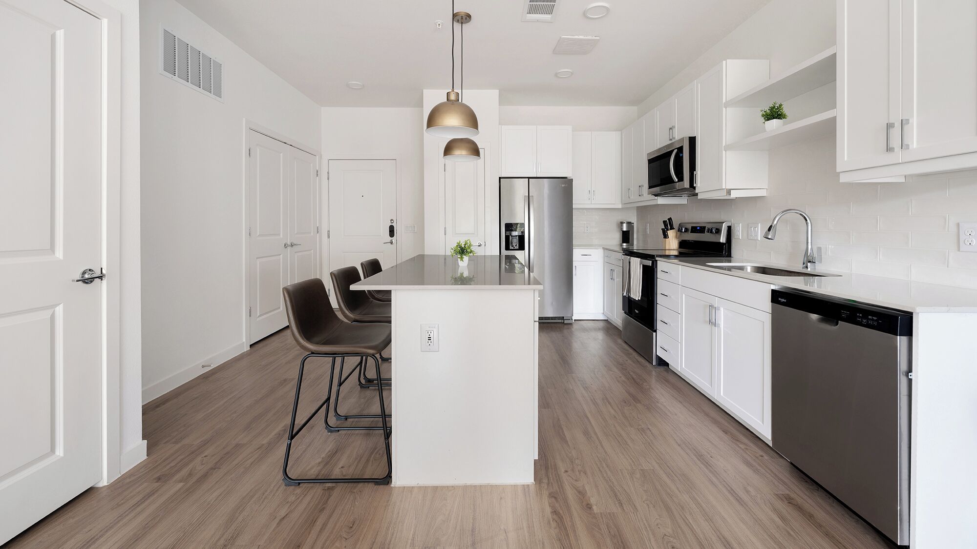 A modern kitchen with white cabinetry, stainless steel appliances, a central island with bar stools, and pendant lighting.