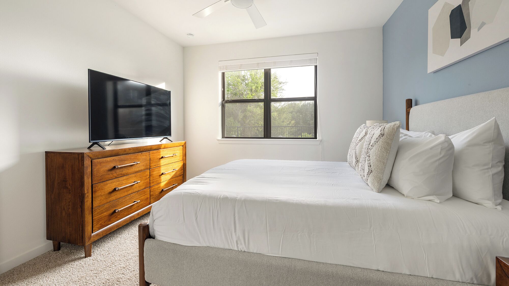 A bedroom with a bed, a wooden dresser, a television, and a window.
