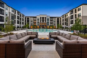 A modern outdoor pool area with a fire pit, lounge chairs, and a poolside seating area. - Landing Furnished Apartments - Belville (Leland)