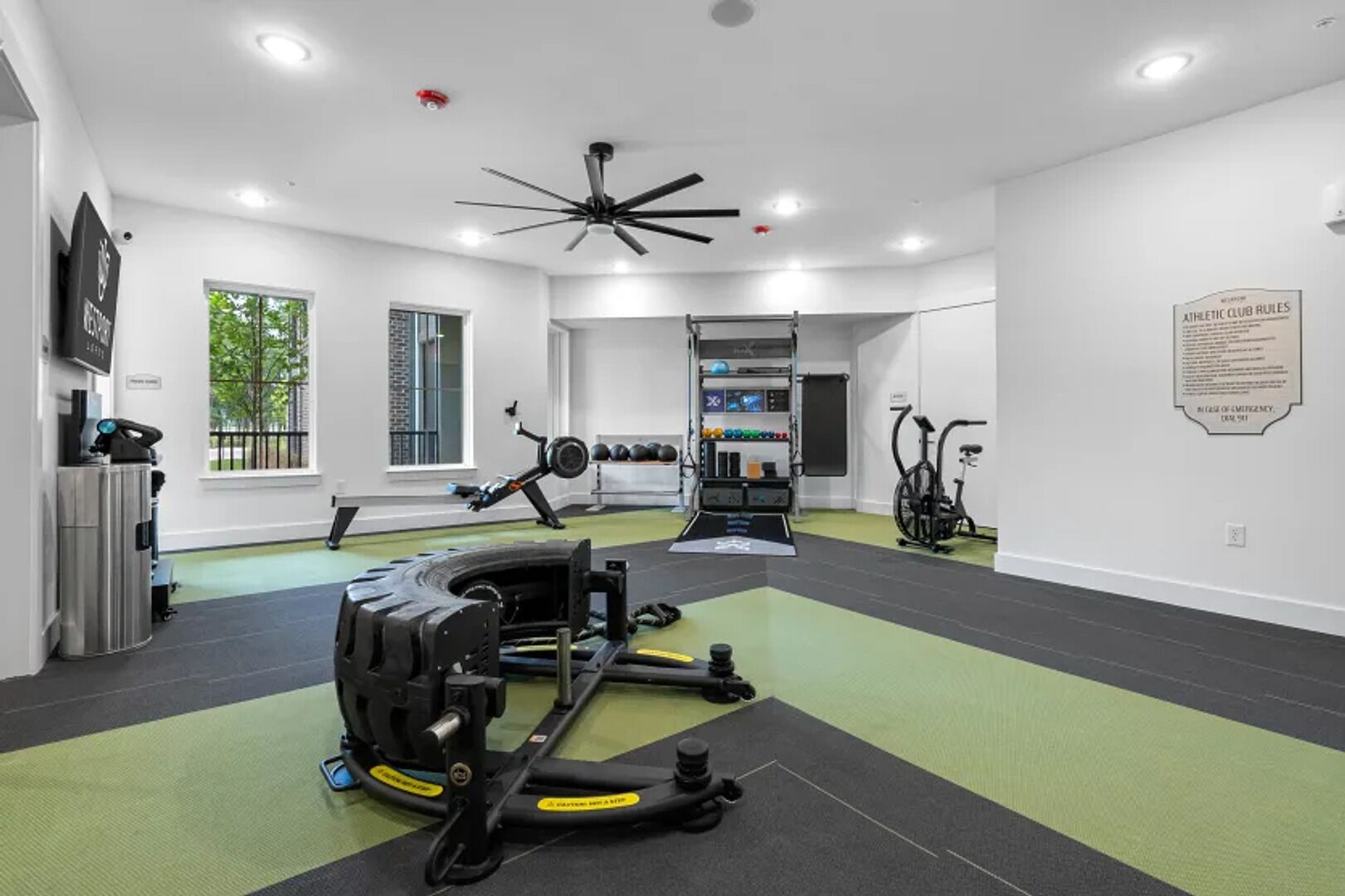 A gym with exercise equipment, a ceiling fan, and a sign with rules.