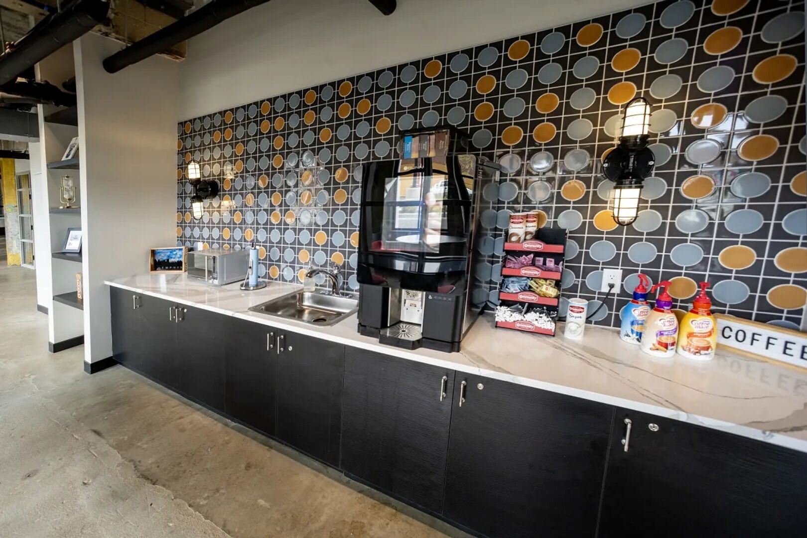 Una cocina moderna con una estación de café, un lavamanos y una pared decorativa con patrones circulares.