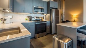 A modern kitchen with grey cabinets, stainless steel appliances, a sink, and a bar area. - Landing Apartments Near Harbor Town (Memphis)