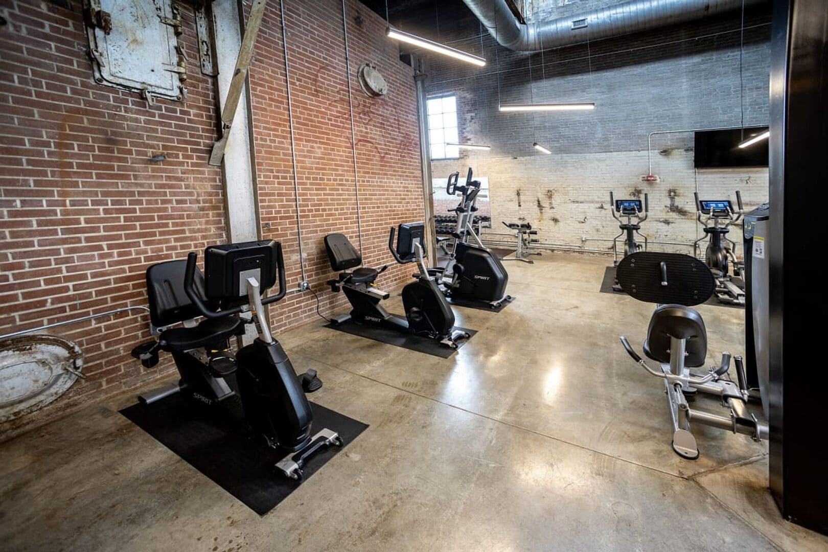 A gym with various exercise equipment, brick walls, and a concrete floor.