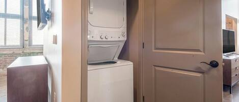A compact laundry room with a washer and dryer, a wooden bench, and a door leading to another room.