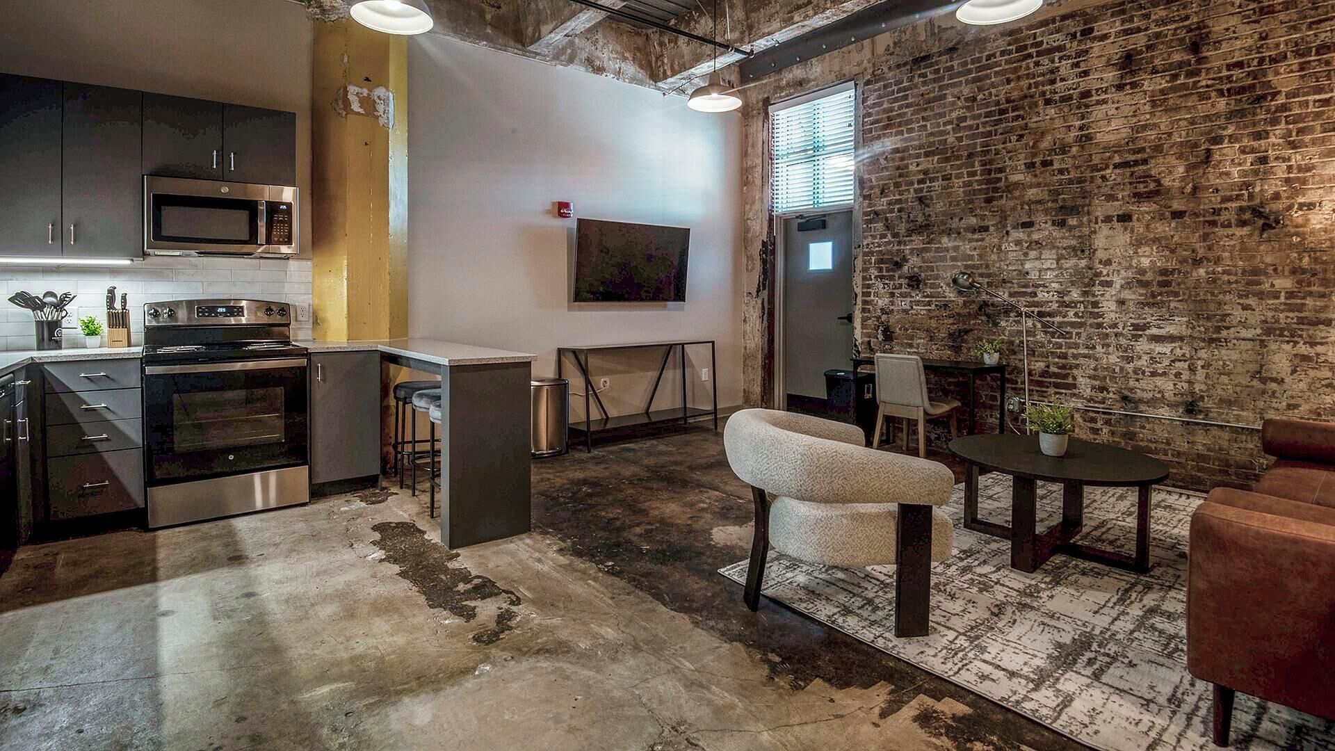 Une cuisine équipée d’appareils modernes, un coin repas avec un mur en briques et un espace détente avec un canapé et une table.