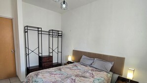 A bedroom with a bed, a nightstand, a hanging light fixture, and a metal shelf unit. - Residencia Puerto Morelos (Puerto Morelos)