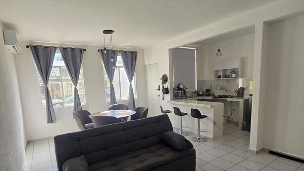 A modern living room with a black sofa, a coffee table, and a dining area with chairs. - Residencia Puerto Morelos (Puerto Morelos)