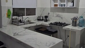 A modern kitchen with a marble countertop, a gas stove, a coffee maker, and a hanging light fixture. - Residencia Puerto Morelos (Puerto Morelos)