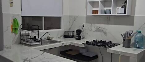 A modern kitchen with a marble countertop, a gas stove, a coffee maker, and a hanging light fixture.