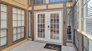 Un edificio con entrada de doble puerta, un felpudo con el texto 'oh hello' y una ventana con persianas.