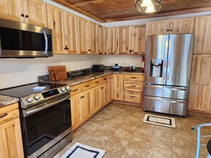 A kitchen with wooden cabinets, stainless steel appliances, a granite countertop, and a tiled floor.